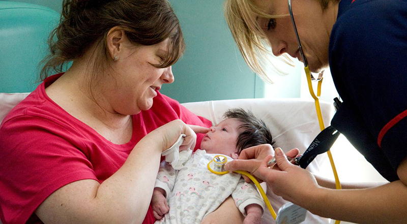 Mew mum holds her baby while a midwife checks the baby's heartbeat